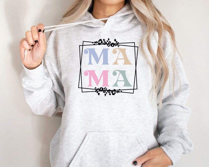May include: A gray hoodie with a black frame and the word "MAMA" in pastel colors. The letters are in a retro font style and are surrounded by a floral design.