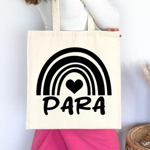 May include: A white tote bag with black text and a rainbow design. The text says "PARA" with a black heart in the centre of the rainbow.