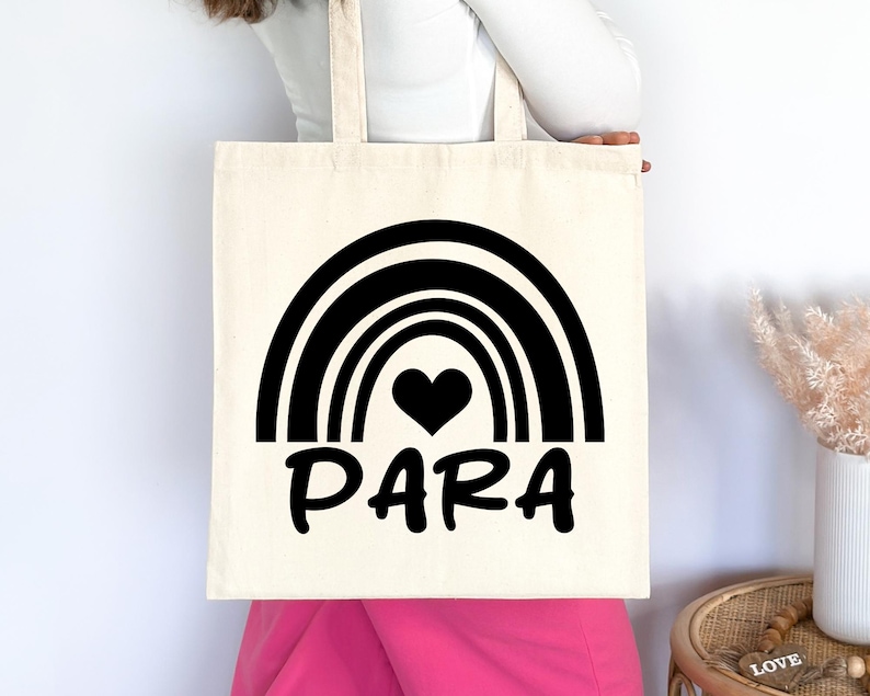 May include: A white tote bag with black text and a rainbow design. The text says "PARA" with a black heart in the centre of the rainbow.