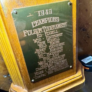 Puede incluir: Un trofeo de madera vintage con una placa de lat&oacute;n grabada. La placa lleva la inscripci&oacute;n "1949 CHAMPIONS FOLSOM TOURNAMENT" y nombres. El trofeo tiene una base de madera oscura y una placa de lat&oacute;n grabada.