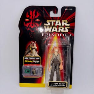 Könnte beinhalten: Eine Star Wars Episode I Actionfigur von Jar Jar Binks in einer transparenten Kunststoffverpackung. Die Verpackung zeigt das Gesicht von Darth Maul und den Text "STAR WARS EPISODE I". Die Figur enthält einen Gungan-Kampfstab und einen CommTech-Chip.