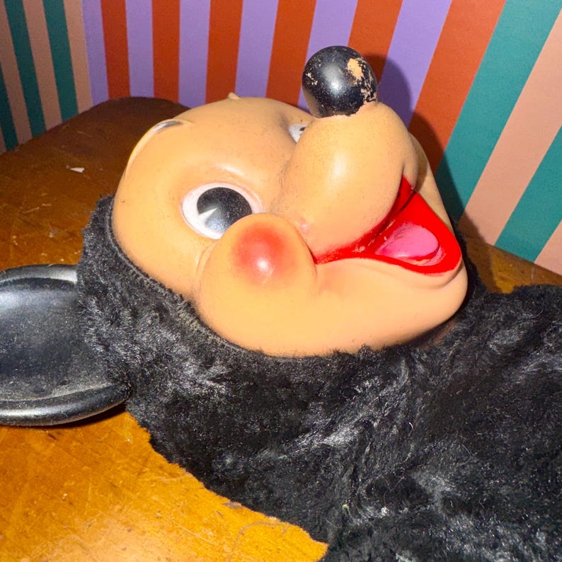 May include: Vintage Mickey Mouse plush toy with a vinyl face, red lips, and a black nose. The plush has a black fur body and a cheerful expression. The toy is a classic collectible.