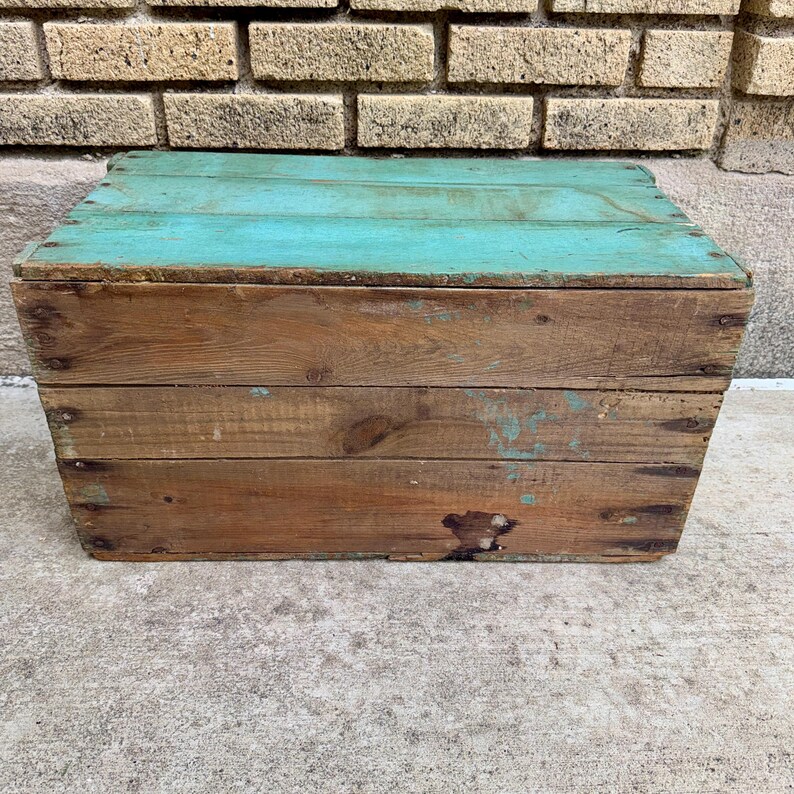May include: A rustic wooden crate with a turquoise painted lid. The crate is constructed from weathered wood planks, showing signs of age and wear. The box is rectangular and appears to be handmade.