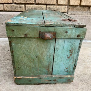 May include: A weathered, rectangular wooden box with a hinged lid. The box is painted in shades of green and turquoise, with visible wear and tear. It features a metal handle and hinges, suggesting an antique or vintage aesthetic. The box is likely used for storage.