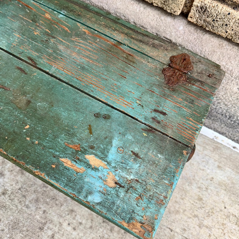 May include: Close-up of a weathered, turquoise-painted wooden surface. The wood shows signs of age with exposed grain, knots, and areas where the paint has chipped away, revealing the natural wood underneath. A rusty metal hinge is visible.