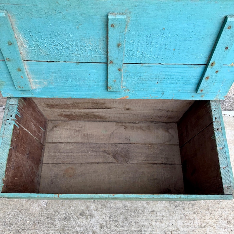 May include: An open, rectangular wooden box with a hinged lid. The exterior is painted a distressed turquoise, while the interior shows natural wood tones. The box is constructed with visible nails and appears to be vintage or rustic.