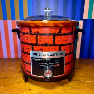 May include: Vintage Hamilton Beach "The Crock Watcher" slow cooker. The red and black appliance features a brick pattern, a glass lid, and a control panel with "Low Cook", "High Cook", and "Auto Shift" settings. A retro kitchen appliance.