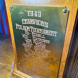 Puede incluir: Un trofeo de madera vintage con una placa dorada. La placa est&aacute; grabada con el texto "1949 CHAMPIONS FOLSOM TOURNAMENT" y enumera nombres. El trofeo est&aacute; montado sobre una base de madera.