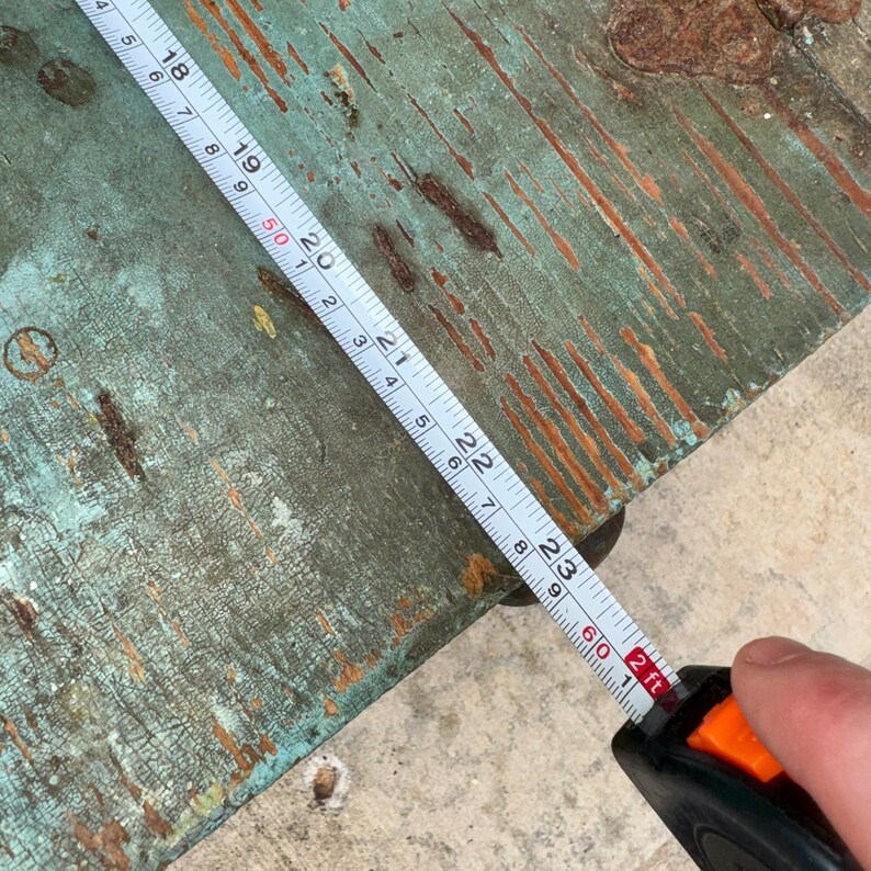 May include: A close-up of a worn, teal-colored wooden surface with a metal tape measure extended across it. The tape measure shows measurements in inches and feet. The wood has visible wear and tear.