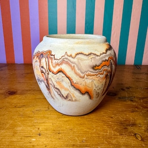 May include: A handcrafted ceramic vase with a unique marbled design. The vase features a cream-colored base with swirling patterns of orange, brown, and tan. The rounded shape and textured surface add to its artistic appeal. This decorative piece is suitable for home decor.