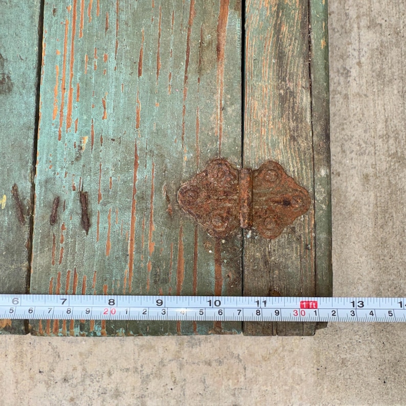 May include: Close-up of a section of a weathered, turquoise-painted wooden surface with visible grain and distressed areas. A rusty, ornate metal hinge is attached. A ruler shows measurements up to 30 inches.