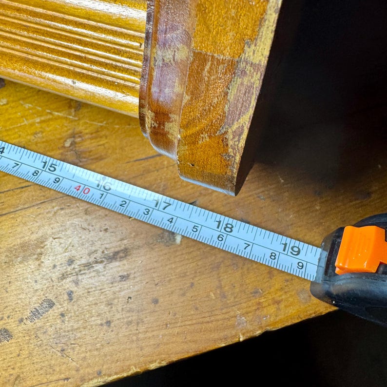 Puede incluir: Primer plano de un mueble de madera con una cinta m&eacute;trica que muestra una medida de aproximadamente 45,7 cm. El mueble es de color marr&oacute;n dorado c&aacute;lido, y la cinta m&eacute;trica es azul y blanca.