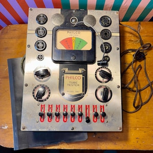 Puede incluir: Probador de tubos Philco vintage, Modelo 060, con una placa frontal de metal plateado. El dispositivo presenta diales, interruptores y un medidor con indicadores rojos, amarillos y verdes. El texto "Philco Tube Tester" es visible.