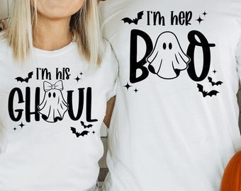 May include: White t-shirts with black Halloween graphics. One says "I'm his Ghoul" with a ghost and bow, the other says "I'm her Boo" with a ghost. Bats and stars are included in the design, perfect for a spooky season.