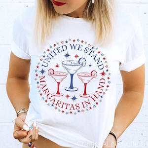 May include: White t-shirt with a red, white, and blue circle design featuring three margarita glasses and the text "United We Stand Margaritas In Hand".
