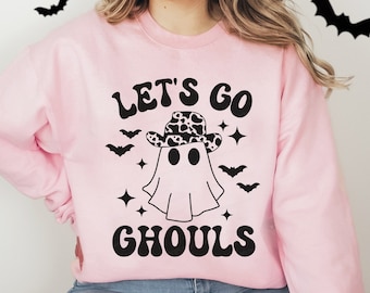 May include: Pink sweatshirt with a black graphic of a ghost wearing a cowboy hat with a cow print design. The text "Let's Go Ghouls" is printed in black on the sweatshirt.