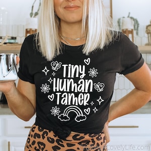 May include: Black t-shirt with white text that reads "Tiny Human Tamer" with a rainbow, hearts, stars, and butterflies.