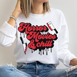 May include: White sweatshirt with a black and red graphic that says "Horror Movies & Chill" with dripping black paint and a red knife and a red cleaver.