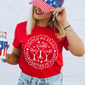 May include: Red t-shirt with a white circle design featuring three margarita glasses and the text "United We Stand Margaritas In Hand".