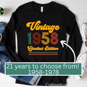 May include: Black long-sleeve shirt with a vintage 1958 design in orange, red, and green. The text "Vintage 1958 Limited Edition" is printed on the shirt. The shirt is laid flat on a white surface with a pair of white sneakers and a pair of blue jeans.