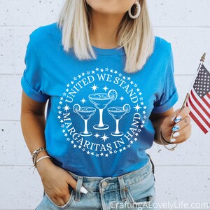 May include: A blue t-shirt with a white circle design featuring three margarita glasses and the text "United We Stand Margaritas In Hand" surrounded by stars.