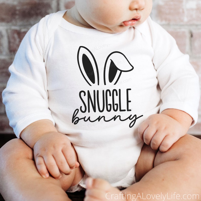 Puede incluir: Unisie blanco para beb&eacute; con orejas de conejo negras y el texto "SNUGGLE bunny" impreso en la parte delantera.
