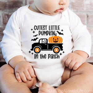 May include: A white long-sleeved onesie with the text "Cutest Little Pumpkin in the Patch" and a black truck with a jack-o-lantern in the bed.
