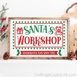May include: A white wooden sign with a red and green Santa's Workshop sign. The sign has a green dotted border and a red ribbon with the text "Handcrafted Toys Since 1703".