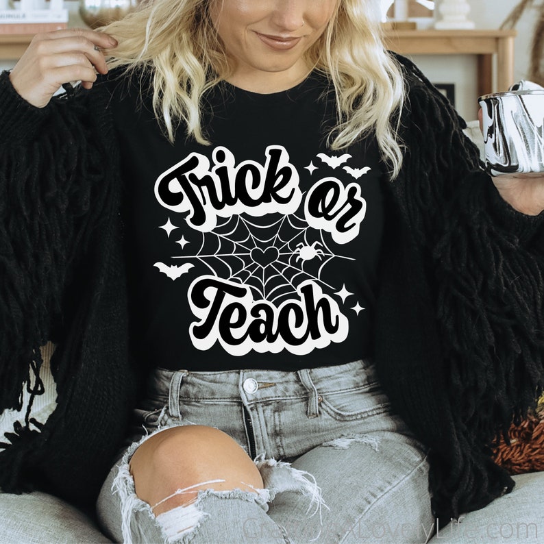 Peut inclure: Un t-shirt noir avec un motif blanc qui dit "Trick or Teach" avec une toile d'araign&eacute;e et des chauves-souris.