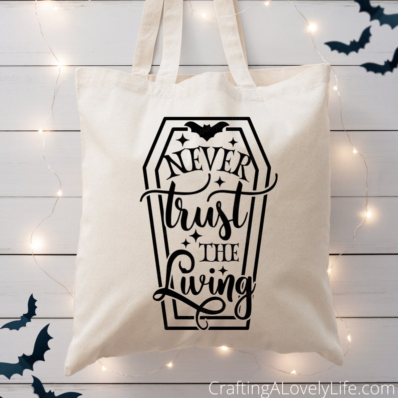 May include: A white canvas tote bag with a black graphic of a coffin with a bat and the text "Never trust the living".
