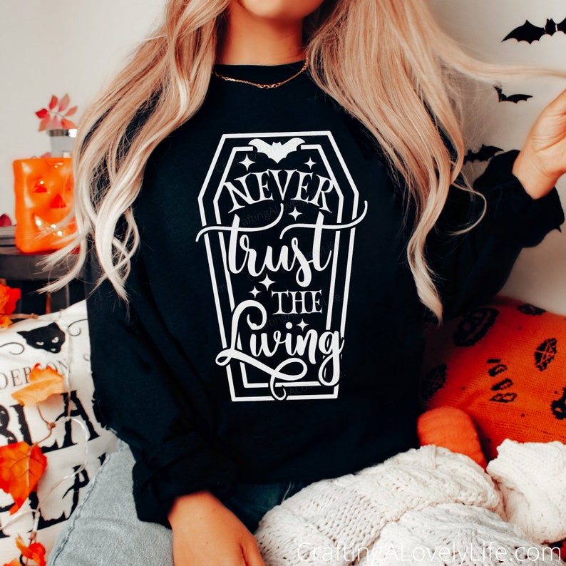 May include: Black sweatshirt with a white graphic of a coffin with the text "Never trust the living" and a bat inside the coffin.