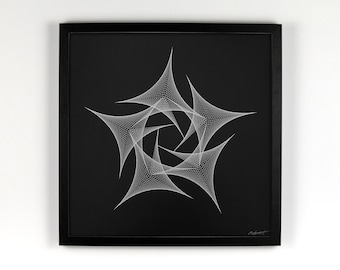 Op de afbeelding: Een ingelijst kunstwerk met een geometrisch ontwerp. Het kunstwerk heeft een zwarte achtergrond met een wit, ingewikkeld, stervormig patroon in het midden. De lijst is zwart en vierkant en het kunstwerk wordt tegen een witte muur getoond.