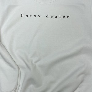 May include: White sweatshirt with the text "botox dealer" printed on the front.