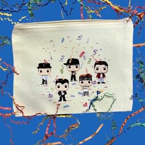 May include: A white canvas zippered pouch with a colorful confetti design and five cartoon figures of people wearing hats. The figures are in a row and are all smiling.