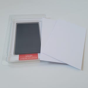 May include: A black ink pad in a clear plastic case with two white cards. The ink pad has a red label that says "STOP! wrong side, turn card over".
