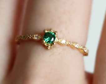 Puede incluir: Un anillo de oro con una piedra preciosa verde y pequeñas piedras blancas engastadas en un diseño delicado y ornamentado. El anillo está en un dedo.