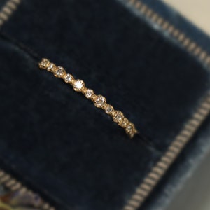 May include: A delicate gold band ring with small round diamonds set in a pave setting. The ring is displayed on a blue velvet cushion.