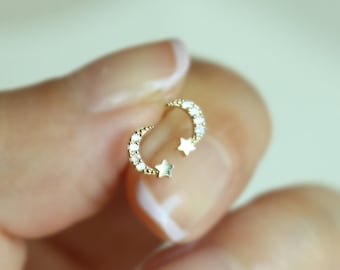 Pode incluir: Um par de brincos de lua crescente de ouro com pequenos detalhes de estrelas e uma fileira de pedras de zircônia cúbica transparentes.