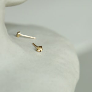 Puede incluir: Un par de pendientes de bot&oacute;n geom&eacute;tricos de oro. Los pendientes son peque&ntilde;os y tienen un dise&ntilde;o facetado.