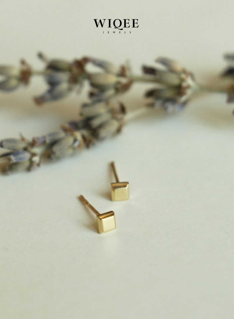 May include: A pair of gold square stud earrings on a white background. The earrings are small and delicate, with a simple design.