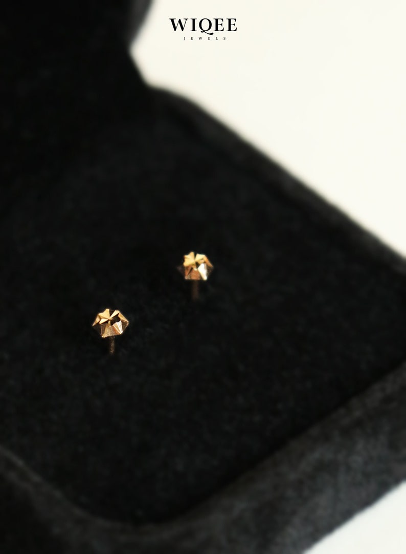 Puede incluir: Dos pendientes de bot&oacute;n de oro con un dise&ntilde;o geom&eacute;trico, presentados en una caja de terciopelo negro. La caja tiene el texto "WIQEE JEWELS" en la parte superior.