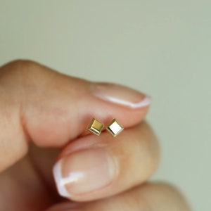 May include: A pair of gold square-shaped stud earrings. The earrings are small and delicate.