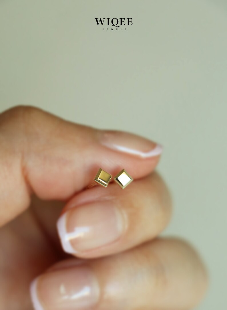 May include: A pair of gold square-shaped stud earrings. The earrings are small and delicate.