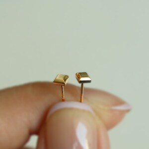 May include: A pair of gold square stud earrings. The earrings are small and simple, with a polished finish.