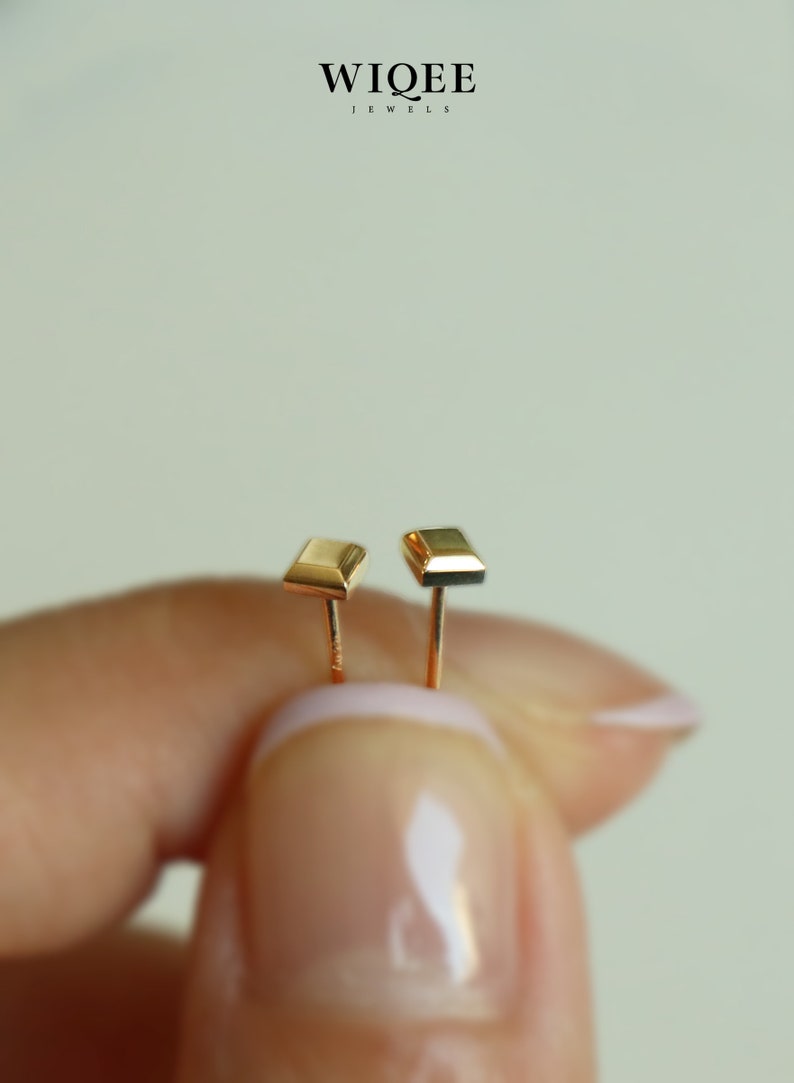 May include: A pair of gold square stud earrings. The earrings are small and simple, with a polished finish.