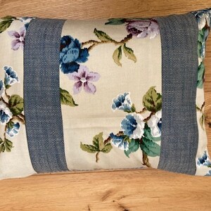 May include: A decorative cushion with a floral pattern in shades of blue, green, and purple on a cream background. The cushion has blue denim fabric strips sewn across the front.