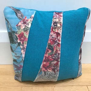 May include: A blue and floral patterned cushion with a geometric design. The cushion is made of a soft, textured fabric.