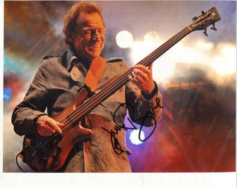 Könnte beinhalten: Farbfotografie eines Musikers, der einen braunen Bassgitarre spielt. Der Musiker trägt eine graue Jacke und einen braunen Gitarrengurt. Der Hintergrund ist mit Bühnenlichtern verschwommen.