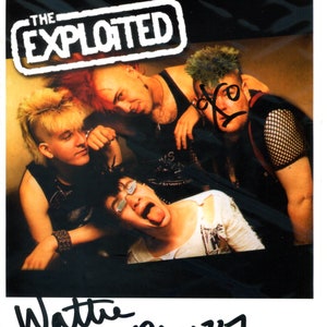 May include: Black and white photo of a punk rock band, The Exploited, with the band name in a black and white box at the top of the image. The band members are wearing black clothing and have mohawks. The photo is signed "Wattie Exploited".