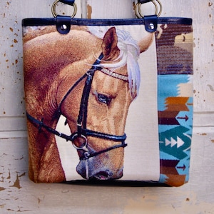 May include: A brown and white horse head tapestry tote bag with blue and brown geometric patterns on the sides. The bag has black leather handles with brass hardware.